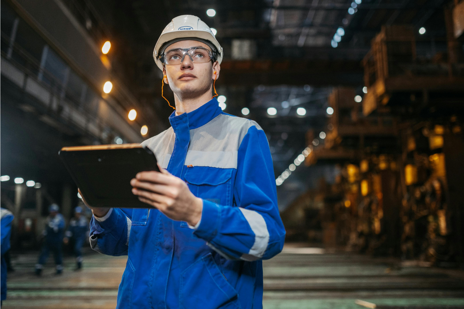 Industrial worker in hard hat and safety glasses reviewing a tablet on a plant floor